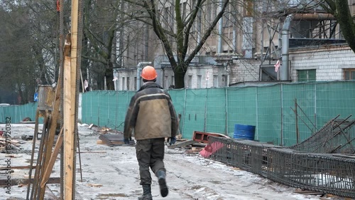 A construction worker walks along the construction site with his back to the camera and moves away
