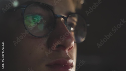 Extreme close-up of teenage boy wearing glasses with screen reflection, focused on computer gaming or watching video
