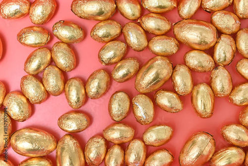 Small pile or group of gold, orange and bronze foil wrapped chocolate easter eggs, against a peach orange background.