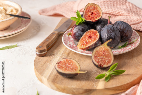 Ripe whole and sliced figs on a plate and a wooden board with a knife and a bowl of crumble in a rustic setting