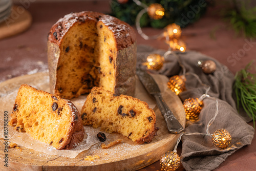 Traditional Italian Panettone, partially sliced and dusted with sugar, displayed on a wooden board surrounded by a cozy brown cloth and decorative golden Christmas lights