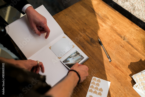 Canvastavla Wedding guests place a printed photo into a minimalist guest book on a wooden table, capturing intimate moments of celebration, memories, and elegant wedding traditions in natural light
