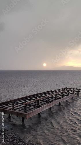 The sun peeking through the clouds after a rainy day, and the abandoned, broken pier. vertical video for social media. 