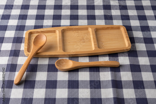 Wooden compartment tray with two spoons on blue and white checkered tablecloth