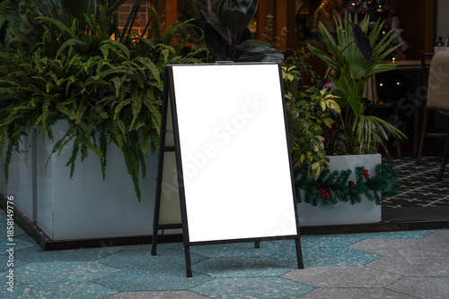 Blank white outdoor advertising stand sandwich board mock up template. Clear street signage board placed by an outdoor dinning area of a restaurant.