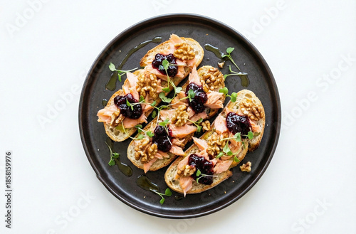 Salmon crostini with blackberry jam and walnuts, on a dark plate, isolated on a white background.