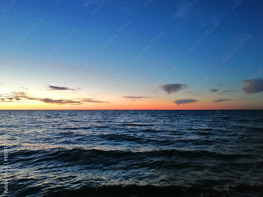Fototapeta premium Sunset over the sea, the sun sets into the clouds behind the horizon