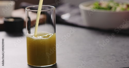 pour apple celery juice in glass on concrete countertop with copy space