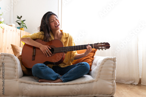 Canvas-taulu Asian woman playing acoustic guitar and singing at home