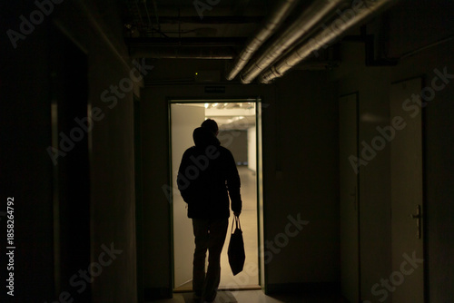 silhouette stepping through bright doorway into warm yellow light, backlit threshold and strong contrast, escape or arrival narrative, pipes overhead create industrial frame, cinematic