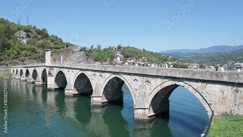 Visegrad, Bosnia and Herzegovina - August 10, 2025: Scenic view of medieval stone arched Mehmed Pasa Sokolovic Bridge spanning Drina River on sunny summer day