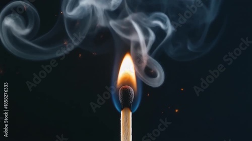 Closeup of a single burning match with bright flame and curling smoke against a dark background.