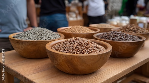 Wooden bowls filled with various seeds and grains are displayed on a market table