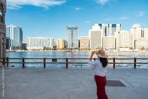 Photography Tourist woman walking through historic Al Seef Dubai with waterfront skyline sho