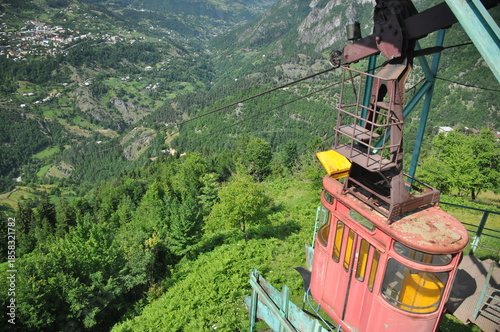 Scenic view from a cable car above a lush green valley in the mountains during a sunny day