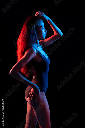 Fashion portrait striking image of a woman in a dark bathing suit, lighting color half lit in red and half in blue studio shot on black background.