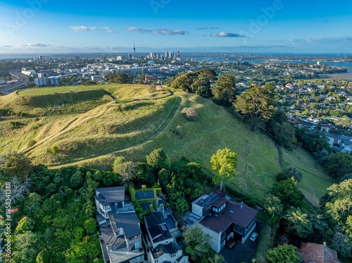 Aerial view of Remuera, Auckland, New Zealand, showcasing the city skyline with the Sky Tower, lush green hills, and residential areas. The image highlights urban living.