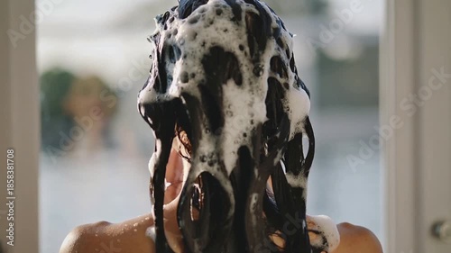 Rear view video of young brunette woman applying creamy shampoo on her wet hair in outdoor shower.Slow motion.AI Generative.