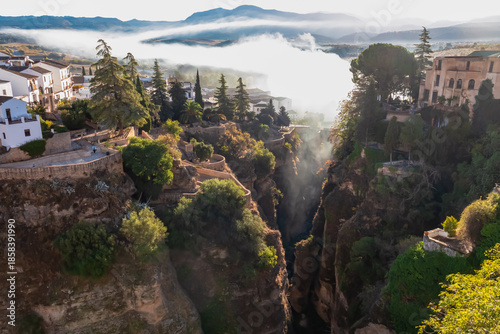 Thick morning mist fills the deep El Tajo gorge below the hanging gardens and white houses of Ronda, Spain, creating a mystical atmosphere around the historic cliffs of this iconic Andalusian city.
