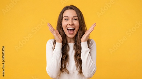 Happy surprised young woman smiling with hands near face on bright yellow background