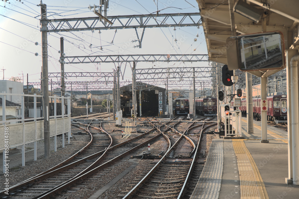 Fototapeta premium 青空の下に広がる鉄道の車両基地と複雑な架線、点検中の電車が停車する車庫の全景を捉えたインフラ風景