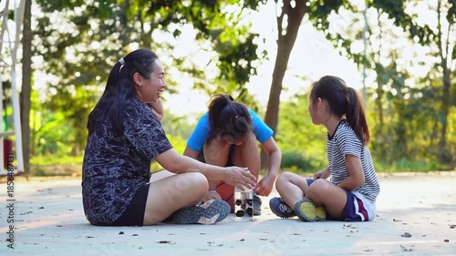 Asian mother and daughters sitting on court, resting and talking after playing basketball.