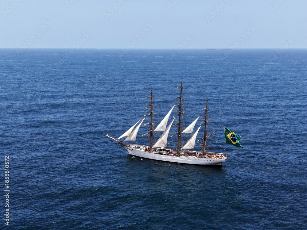 Fototapeta premium Aerial view of a three-masted sailing ship with sails and a large Brazilian flag on the stern sailing in the Atlantic Ocean. The training ship of the Brazilian Navy.