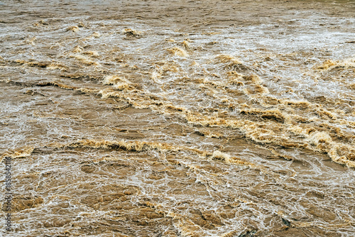 Smudged water flows profusely. River water flowing profusely. Flood waters rushing down river after storm flows through. Turbulent river dam. Water turbulence of river due to dam. Water Nature Texture