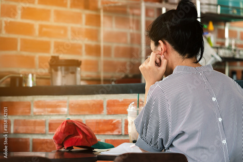Young asian woman looking reading book and taking notes in cafe. Serious female student is sitting reading textbook preparing for exams. Female student stressed out and focused studying for exam.