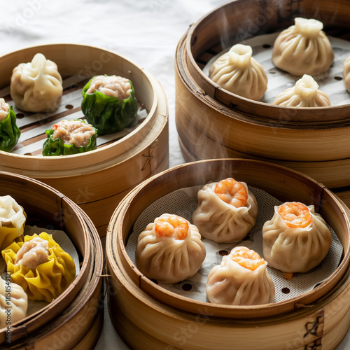 Assorted gourmet dim sum in bamboo basket, delicate translucent wrappers, juicy fillings, white backdrop, ultra-realistic textures, appetizing styling, 8k photorealistic stock food image.