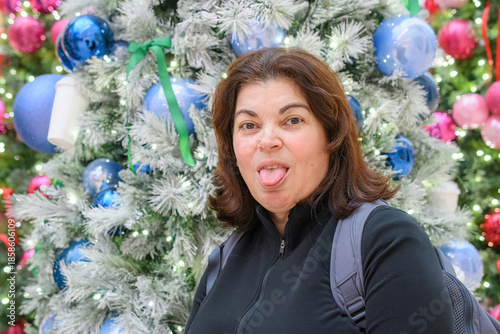 Woman playfully sticking out her tongue in front of a decorated Christmas tree.