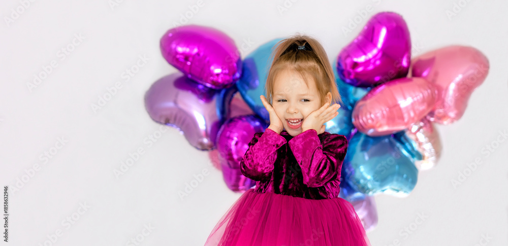 Fototapeta premium A banner dedicated to Valentine's Day, with a place to copy the text. A sweet happy little girl in a bright purple dress. Foil heart-shaped multicolored balloons