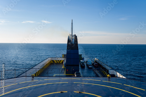 Photos A wide view from the upper deck of a ferry shows vehicles parked below and geometric safety markings, with open blue water stretching to the horizon under clear daylight