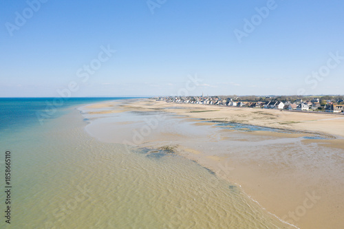 Wallpaper Mural Wide sandy beach at low tide stretches along Bernieres-sur-Mer, with calm turquoise sea and a row of coastal houses under a clear blue sky. Torontodigital.ca