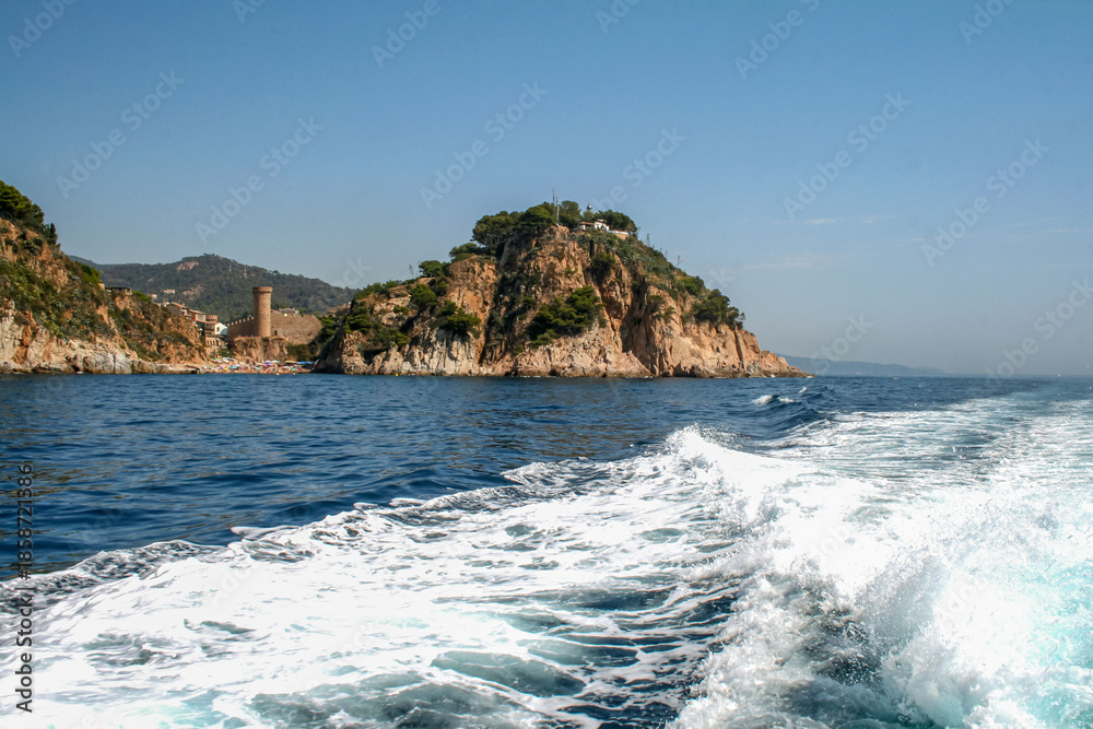 Fototapeta premium Sunny day on the Mediterranean coast with rocky cliff, historic tower, and blue sea. Idyllic travel scenery in Spain, vibrant beach, clear sky, and summer vacation destination.