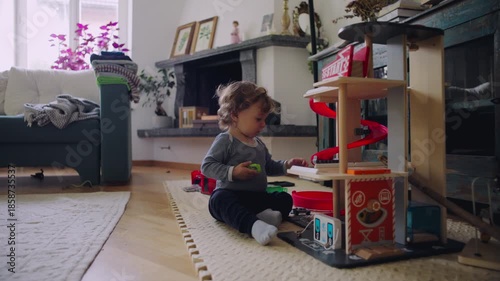 Toddler sitting beside toy garage interacting with playset showing curiosity coordination and independent imaginative play at home