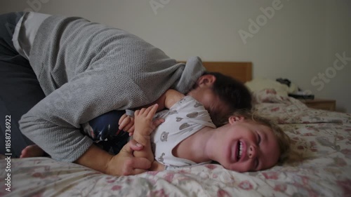 Woman playfully tickling toddler on bed during intimate family moment, joy, laughter, trust, affection, emotional bonding, everyday parenting connection inside home