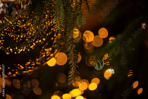 Close-up of a Christmas tree branch with a glass ornament and glowing festive lights. Warm golden bokeh creates a cozy, magical holiday atmosphere and seasonal background.