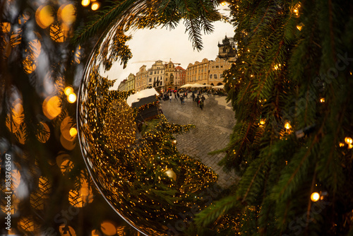 Reflection of a Christmas square in Prague captured inside a glass ornament on a Christmas tree. Festive lights and warm bokeh create a magical holiday atmosphere in the city center.