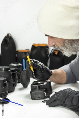Technician repairing DSLR camera with precision tools, lenses and cleaning equipment. Concept of photography service, camera maintenance, repair workshop, technology care.