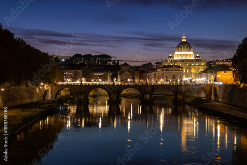 View of St. Peter's Basilica in Vatican City and the Sant'Angelo Bridge and the Tiber River, from the Umberto I Bridge, at dusk in Rome, Italy.