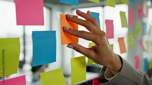 Woman Sticking Colorful Sticky Notes on Glass Board in Office