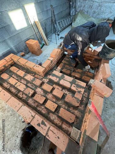 Worker laying brickwork for a heating stove. Building the ash pit. Smoke channels of the stove bench laid with brick are visible. Stove construction.