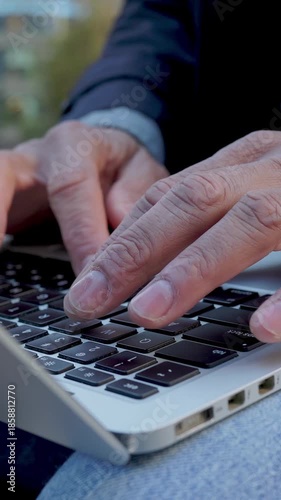 Close-up of adult man typing on laptop outdoors. Focused professional working digitally in an urban park. Business and technology concept.