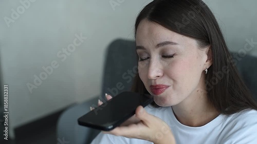 young beautiful caucasian brunette woman recording voice message, smiling widely, casual clothes, white T-shirt, talking by smartphone