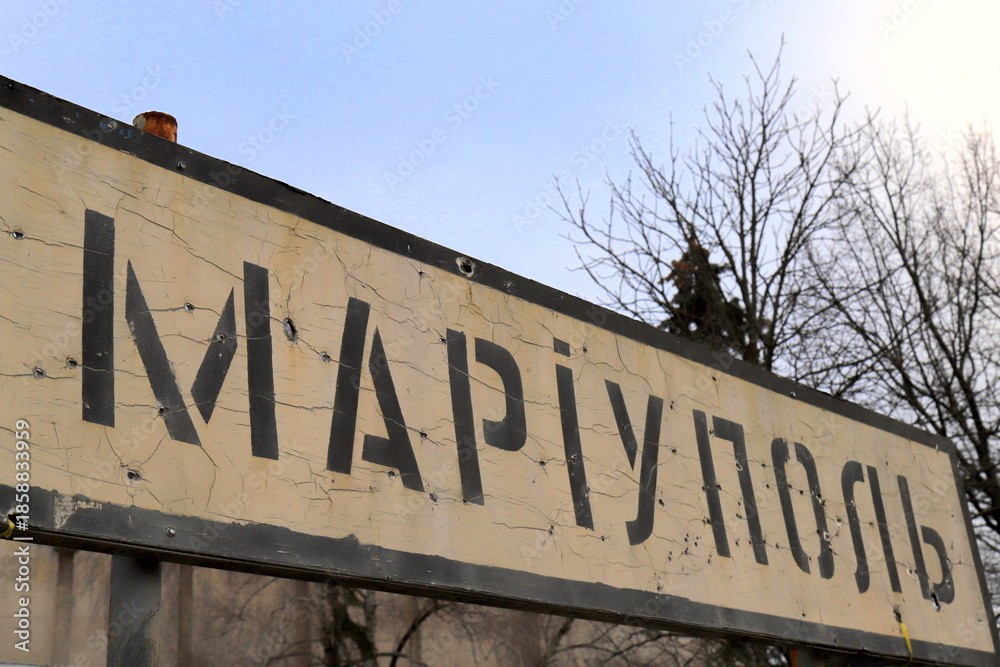 Obraz premium War in Ukraine. A road sign with inscription in Ukrainian - Mariupol, pierced by bullets during war in Ukraine.