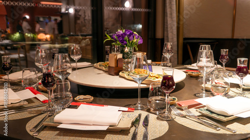 Luxury restaurant round table set for group dining with wine glasses, purple flower centerpiece and Turkish tea creating elegant atmosphere