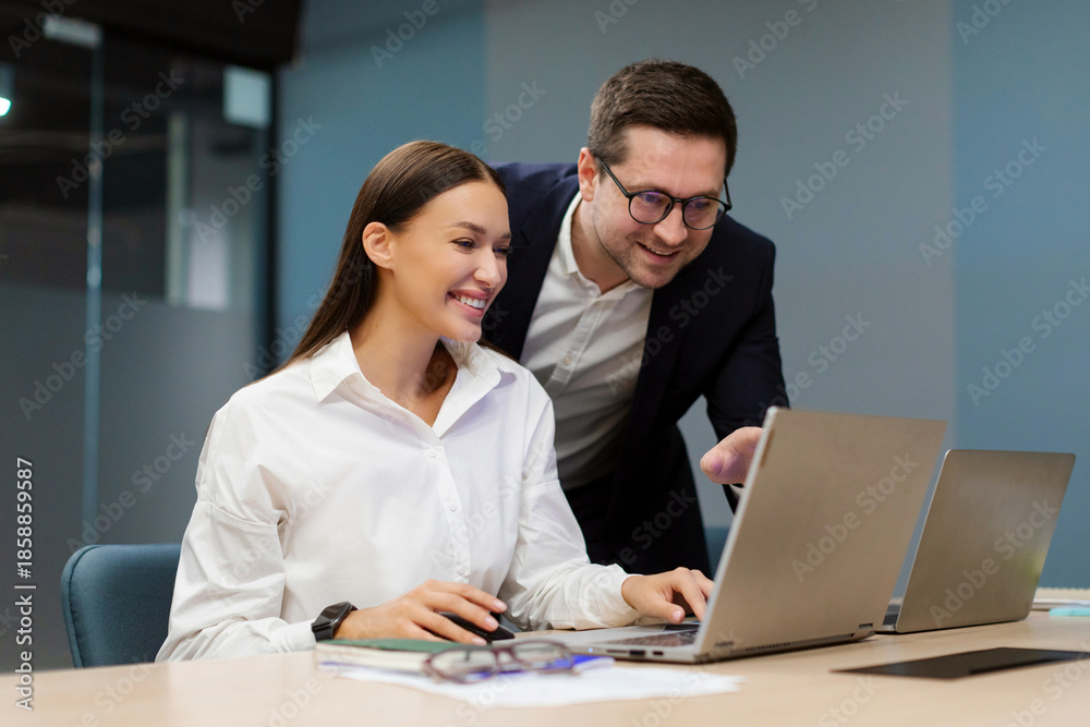 Obraz premium Positive European businesspeople discussing goals and plans during meeting together in modern office, sitting at desk and using laptop