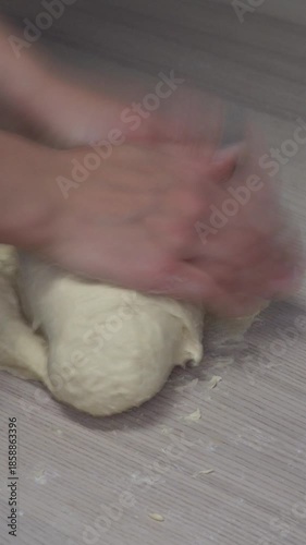 Hands kneading dough on kitchen table, homemade cooking process, traditional food preparation, close up manual dough mixing, rustic home kitchen. 9:16