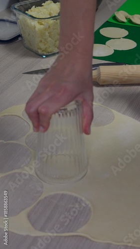 Cutting dough circles with glass for dumplings, traditional homemade food preparation, close up kitchen process, manual cooking technique. 9:16